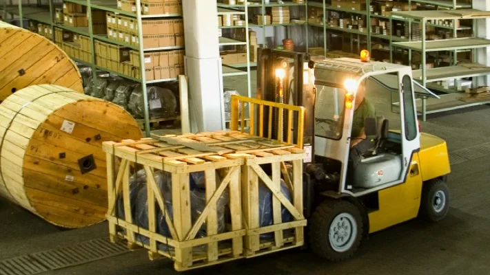 Camera view of the receiving area: a forklift carries a crated pallet past cable drums